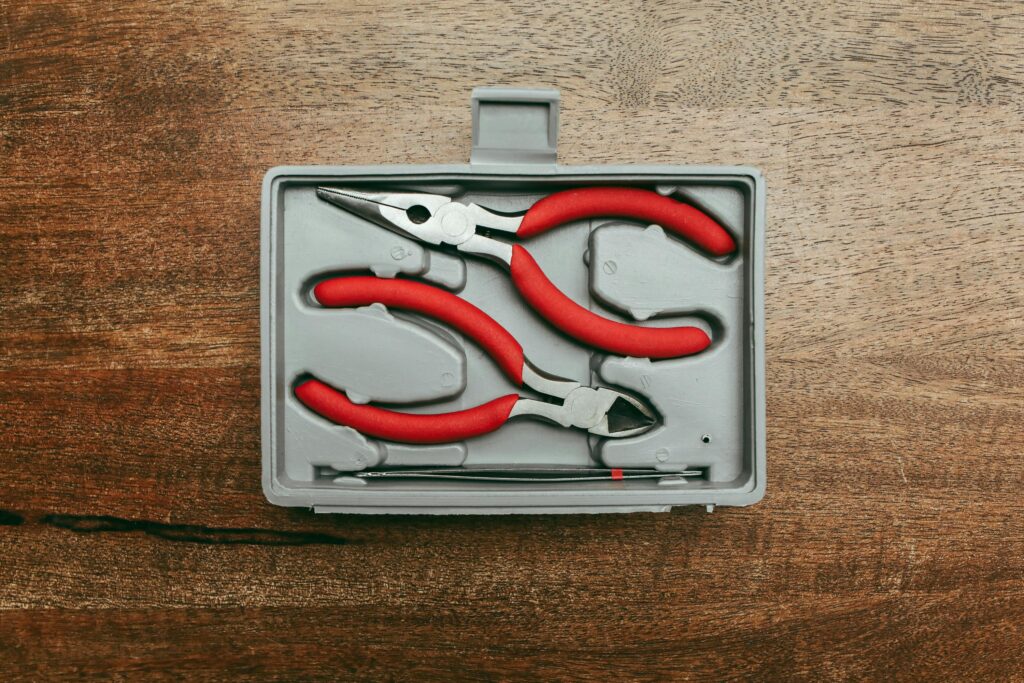 Top view of a red handled pliers set in a box on a wooden surface.