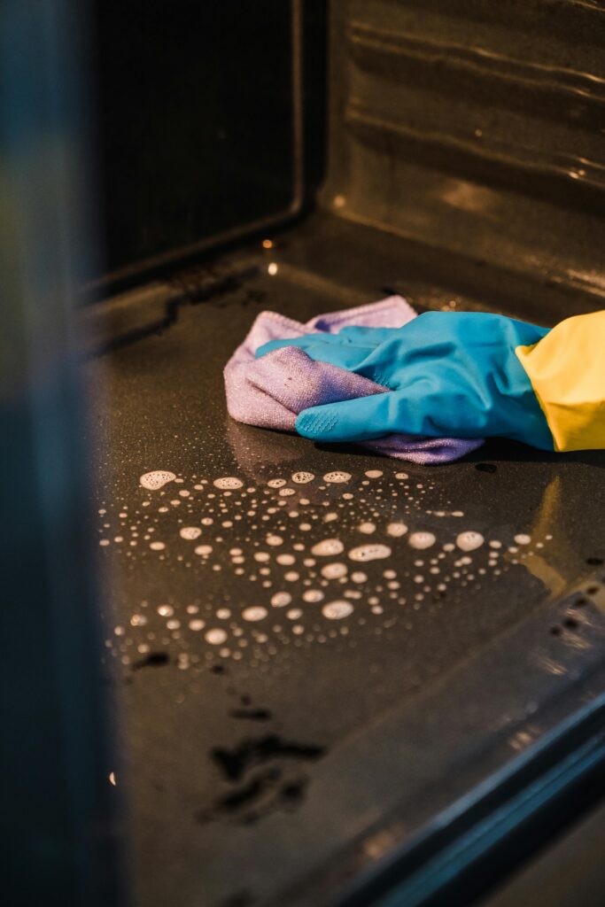 A gloved hand cleans an oven interior using a soapy cloth for a spotless finish.